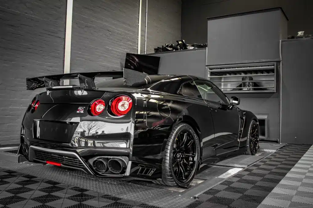 Schwarzer Sportwagen mit großen Felgen und Heckspoiler auf einem Leistungsprüfstand.
